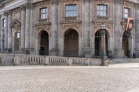 a large old building with columns and arched pillars is in the center of a cobblestone street