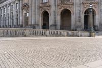 a large old building with columns and arched pillars is in the center of a cobblestone street