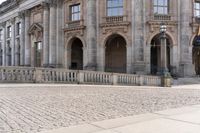 a large old building with columns and arched pillars is in the center of a cobblestone street