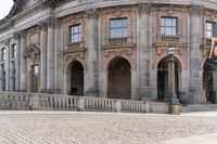 a large old building with columns and arched pillars is in the center of a cobblestone street