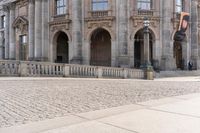 a large old building with columns and arched pillars is in the center of a cobblestone street