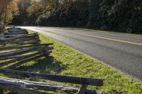 some split rail wooden fence sitting by the street in front of trees and a road