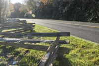 some split rail wooden fence sitting by the street in front of trees and a road