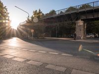 a street with a crosswalk at an intersection in front of a bridge at sunset