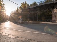 a street with a crosswalk at an intersection in front of a bridge at sunset