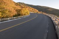 an empty roadway on a mountain slope with the sun in the distance in the fall