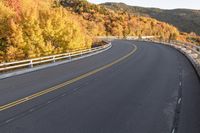 an empty roadway on a mountain slope with the sun in the distance in the fall