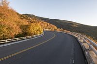 an empty roadway on a mountain slope with the sun in the distance in the fall