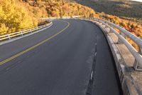 an empty roadway on a mountain slope with the sun in the distance in the fall