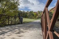 a wooden bridge over a paved path in the autumntime with fall foliage and a path winding through it