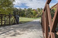 a wooden bridge over a paved path in the autumntime with fall foliage and a path winding through it