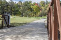 a wooden bridge over a paved path in the autumntime with fall foliage and a path winding through it