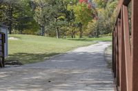 a wooden bridge over a paved path in the autumntime with fall foliage and a path winding through it