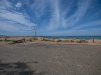 a street sign on a beach near water and some clouds in the blue sky with a white flag