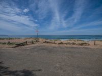 a street sign on a beach near water and some clouds in the blue sky with a white flag