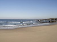 a lone beach with ocean waves breaking into the shore and sand in front of the ocean