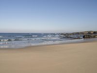 a lone beach with ocean waves breaking into the shore and sand in front of the ocean