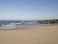 a lone beach with ocean waves breaking into the shore and sand in front of the ocean