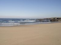 a lone beach with ocean waves breaking into the shore and sand in front of the ocean