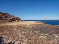 rocks, water and blue sky surround the beach near rocks and small sand - covered shoreline