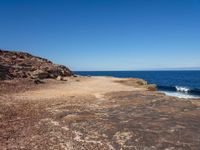 rocks, water and blue sky surround the beach near rocks and small sand - covered shoreline