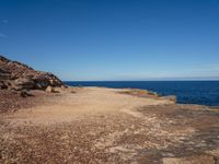 rocks, water and blue sky surround the beach near rocks and small sand - covered shoreline