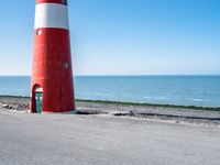 two people on bikes approaching a red and white lighthouse by the water with no one on them