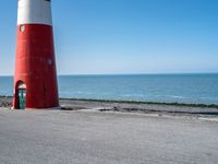 two people on bikes approaching a red and white lighthouse by the water with no one on them