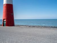 two people on bikes approaching a red and white lighthouse by the water with no one on them