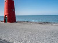 two people on bikes approaching a red and white lighthouse by the water with no one on them