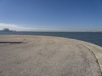 a lone beach sits near the ocean with a bench at one end of it that's facing a city skyline