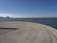 a lone beach sits near the ocean with a bench at one end of it that's facing a city skyline