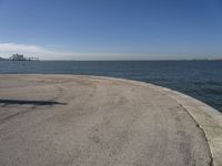 a lone beach sits near the ocean with a bench at one end of it that's facing a city skyline