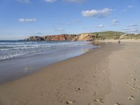 people are on the beach with the tide coming in and footprints in the sand leading to the ocean