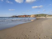 people are on the beach with the tide coming in and footprints in the sand leading to the ocean