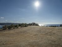 a motorcycle on dirt road near the ocean under sun light and blue skies, on a sunny day