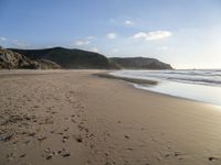 two people are walking along a sandy beach and some hills and blue water there is a sign that says go