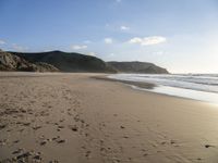 two people are walking along a sandy beach and some hills and blue water there is a sign that says go