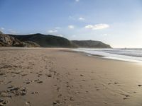 two people are walking along a sandy beach and some hills and blue water there is a sign that says go