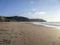 two people are walking along a sandy beach and some hills and blue water there is a sign that says go
