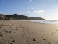 two people are walking along a sandy beach and some hills and blue water there is a sign that says go