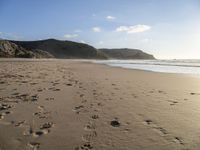 two people are walking along a sandy beach and some hills and blue water there is a sign that says go