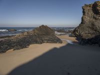 rocks on the beach in the background and sand in the foreground with a body of water