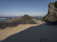 rocks on the beach in the background and sand in the foreground with a body of water