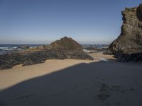 rocks on the beach in the background and sand in the foreground with a body of water