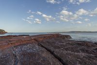 rocks that are sitting on the shore of the water with a small plane flying in the distance