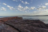 rocks that are sitting on the shore of the water with a small plane flying in the distance