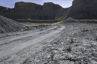 dirt road leads to large rocks in a badlands landscape, with a sign posted at the end