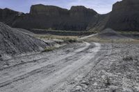 dirt road leads to large rocks in a badlands landscape, with a sign posted at the end