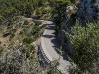 a motorcycle is driving down the middle of a mountain pass surrounded by trees and hills